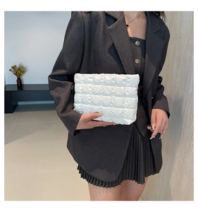 Dettaglio di una pochette trapuntata bianca tenuta da una modella in un blazer grigio