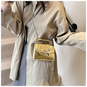 Detail view of golden shiny crossbody bag with star metal ornament and silver chain strap