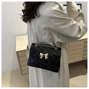 Close-up of elegant black quilted crossbody bag with golden bow and chain strap