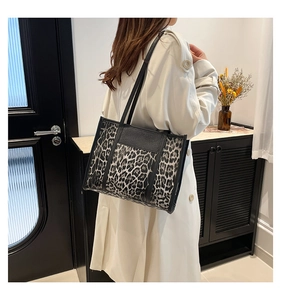 Détail d'un sac cabas imprimé léopard avec bandoulière en cuir noir porté par un mannequin