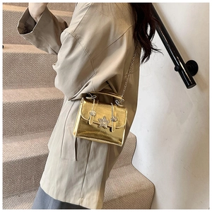 Detail of a shiny gold shoulder bag with star-shaped buckle and metal chain strap