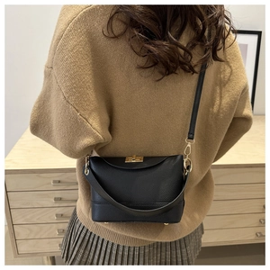 Détail d'un sac bandoulière en cuir grainé noir avec fermoir doré porté par un mannequin