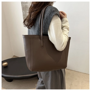 Detailed view of dark brown leather tote bag with vertical stitching on model shoulder