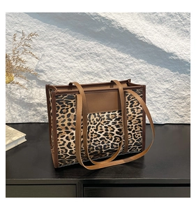 Détail du sac cabas léopard avec anses en cuir marron posé sur une surface en bois sombre