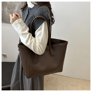 Detail of dark brown leather tote bag worn by model, focusing on texture and shoulder strap