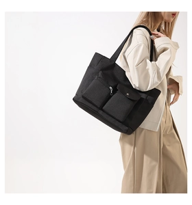 Detail view of black nylon tote bag featuring functional external zip and flap pockets