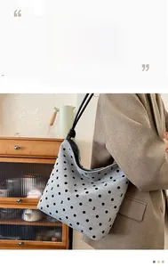 Detail of grey canvas tote with black polka dots and slim straps worn by a model
