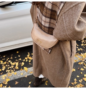 Beige faux leather hobo bag worn with a brown coat over a scenic autumn street