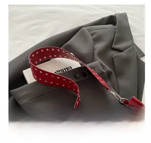 Détail du sac rouge en cuir avec large bandoulière à rivets argentés sur un blazer