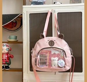 Detail of pink canvas tote bag with clear pocket showing plush bear and badges