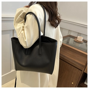 Minimalist black leather tote bag worn by a model in a cozy interior setting