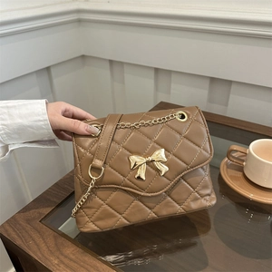 Brown quilted crossbody bag with golden bow and chain strap on a wooden table