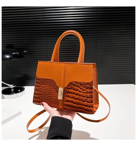 Detail showing the brown crocodile-embossed leather texture and gold metal lock of the handbag