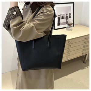 Minimalist black leather tote bag with vertical stitching shown on model in trench coat