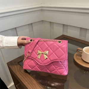 Pink quilted chain crossbody bag with a gold bow accent on a wooden table setup