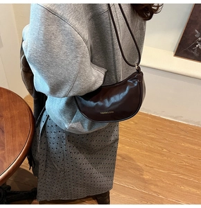 Detail of a dark brown crescent leather bag worn over the shoulder in a warm indoor setting