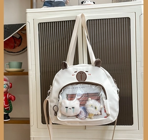 Detail of white canvas crossbody bag with brown bear embroidery and a clear PVC zip pocket