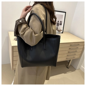 Detailed view of black matte leather tote bag with long handles in a minimalist interior