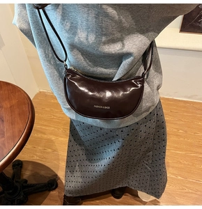 Detail of dark brown glossy leather saddle bag with silver lettering and shoulder strap