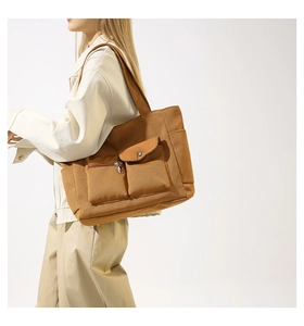 Detail view of khaki nylon tote bag featuring front zipper and buckle functional pockets