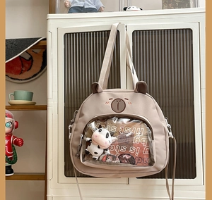 Detail view of beige canvas cartoon bear bag with transparent window and plush cow toy