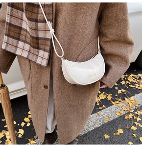 Detailed view of white half-moon crossbody bag with knot shoulder strap on brown coat