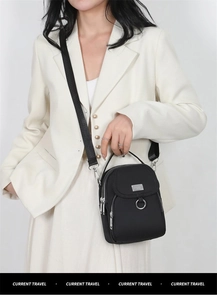 Detail view of a black nylon crossbody phone bag with double zippers and adjustable strap