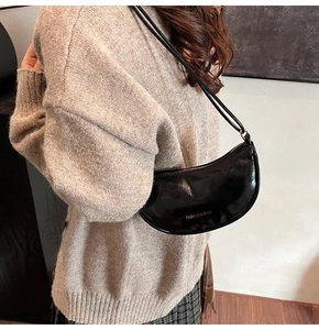 Detail of glossy black crescent shoulder bag with golden text on beige knit sweater