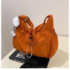 Detail of orange nylon pleated crossbody bag with plush rabbit charm and wide strap