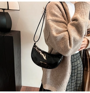 Detail of black patent leather half-moon bag with golden FASHION & BAGS text logo