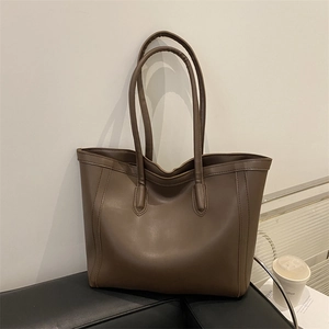 Minimalist brown large capacity leather tote bag for women on a sleek black sofa