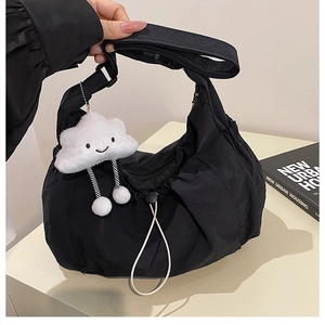 Detail of black nylon shoulder bag featuring pleats, drawstrings and a white plush charm