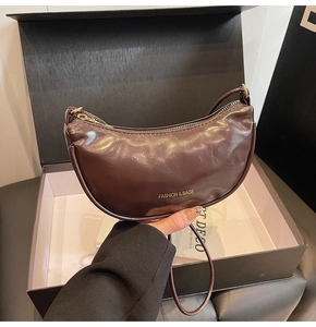 Detailed close-up of dark brown half-moon bag with golden lettering in gift box