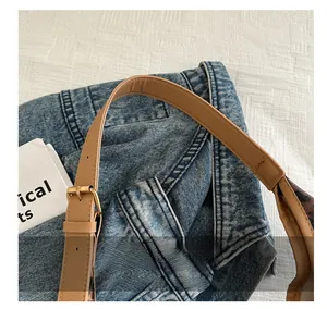Détail de la bandoulière en cuir marron et boucle en métal sur le sac cabas en denim