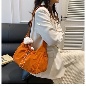 Detail of vibrant orange nylon shoulder bag with drawstring closure and plush cloud charm