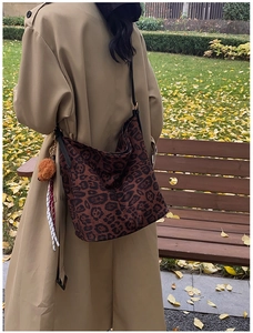 Outdoor shot of a leopard print tote bag with plush bear charm and sleek black straps