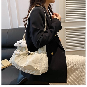 Close-up of beige nylon crossbody bag with drawstring detail and cloud plush charm