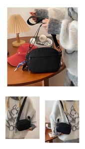 Detail view of black nylon crossbody bag with adjustable strap and braided charm accent