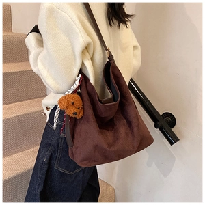 Close-up of brown suede tote bag featuring a teddy bear charm and patterned silk scarf