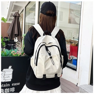 Rear view of a white nylon school backpack with multi-pocket design on female model