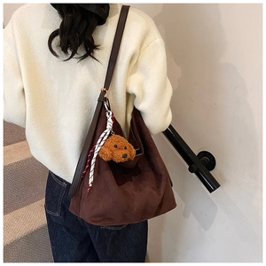 Detail view of large brown suede tote bag with silk scarf and teddy bear charm accessory