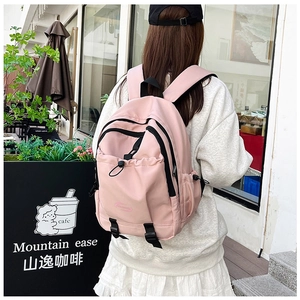 Outdoor shot of a pink nylon school backpack featuring multiple zippered compartments