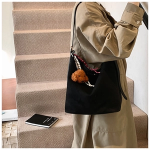 Close-up of black suede tote bag featuring a cute brown teddy dog plush pendant and woven cord