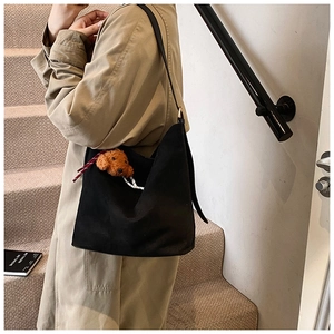 Close-up of black tote bag with cute plush puppy charm worn with beige trench coat