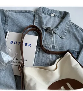 Detail of minimalist cream canvas tote bag with brown leather strap on denim jacket