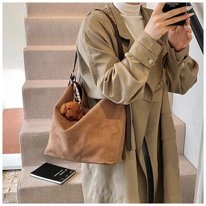 Detail of brown suede tote bag with plush teddy charm and silk scarf on a model's shoulder