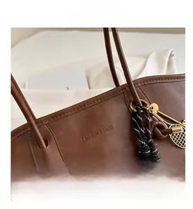 Dettaglio della borsa tote in pelle PU marrone con logo a rilievo e ciondolo a racchetta