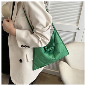 Detail shot of green quilted triangle tote bag worn over a white suit jacket