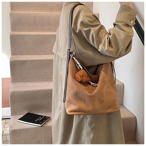 Detail of a large brown suede hobo bag featuring a plush bear charm and patterned scarf decor