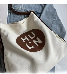 Close-up of canvas tote bag with brown leather HULN logo patch on denim background
